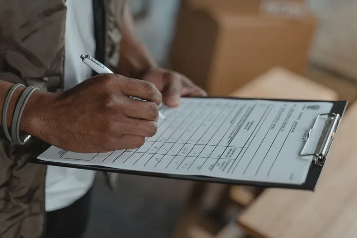Mão preenchendo um formulário de verificação preso a uma prancheta